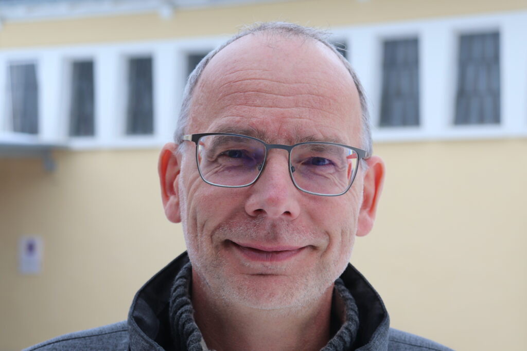 Mann mit Brille vor gelbem Gebäude im Freien