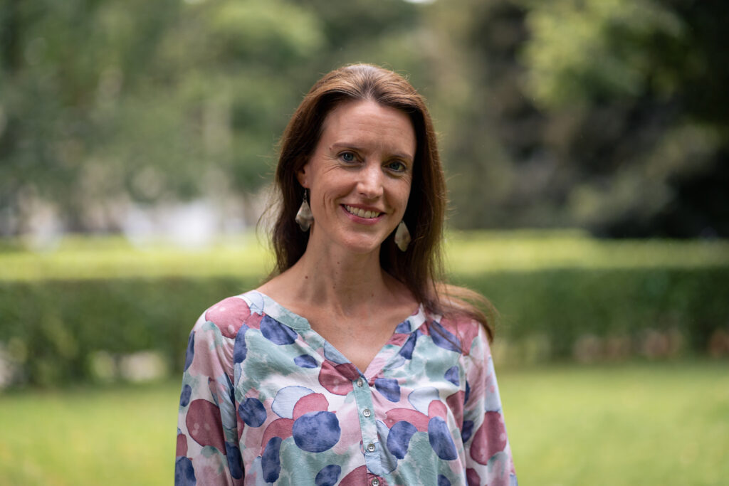 Frau lächelt im Garten mit buntem Hemd.