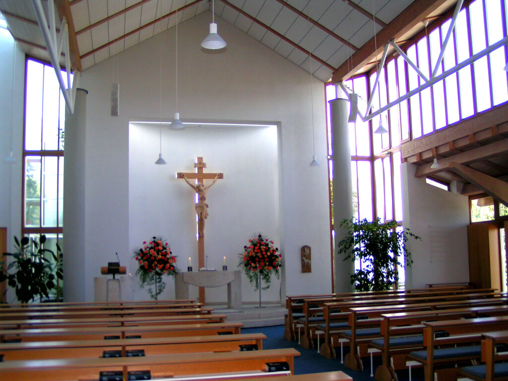 Moderner Kircheninnenraum mit Holzbänken und großem Kreuz