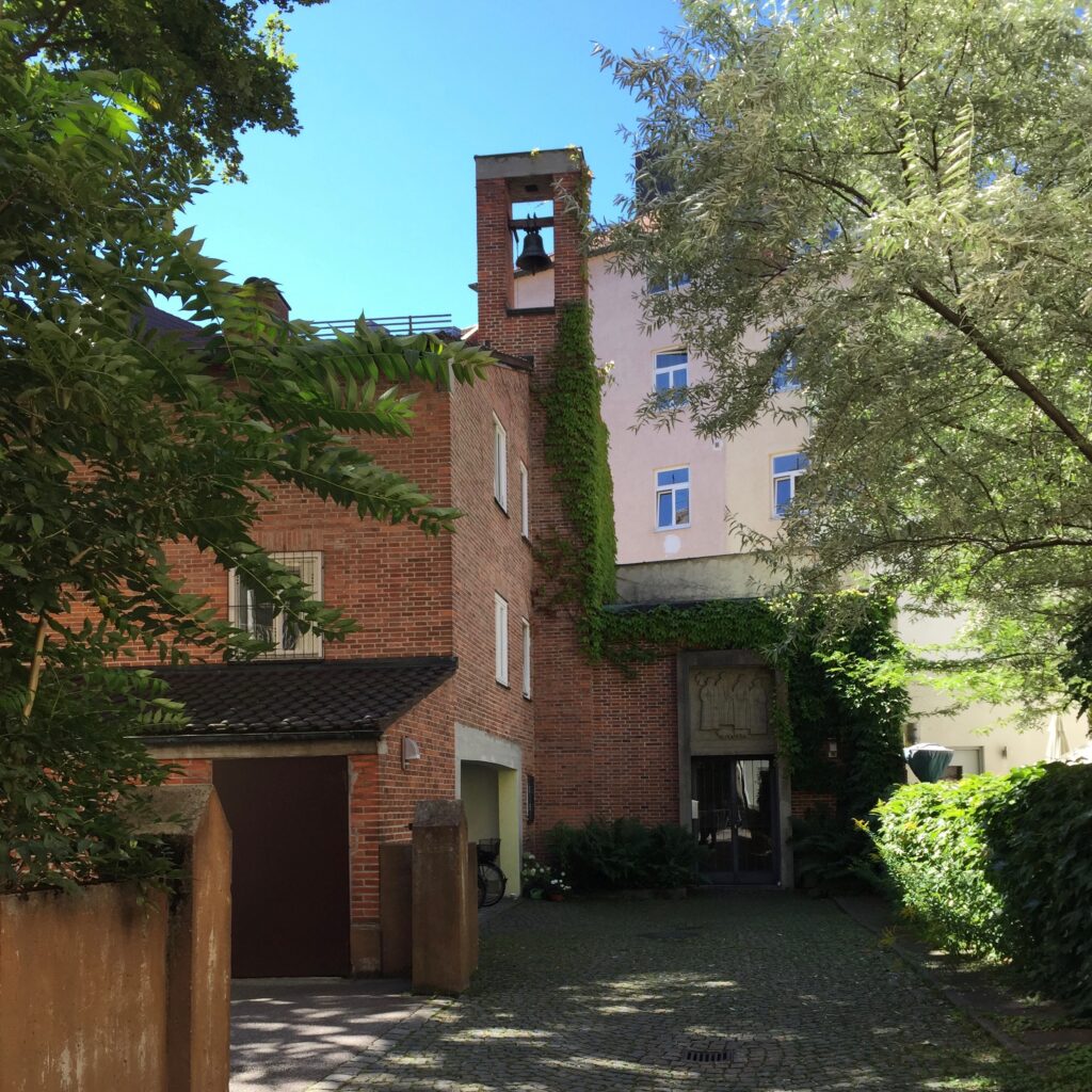 Ziegelgebäude mit Glockenturm und grüner Umgebung