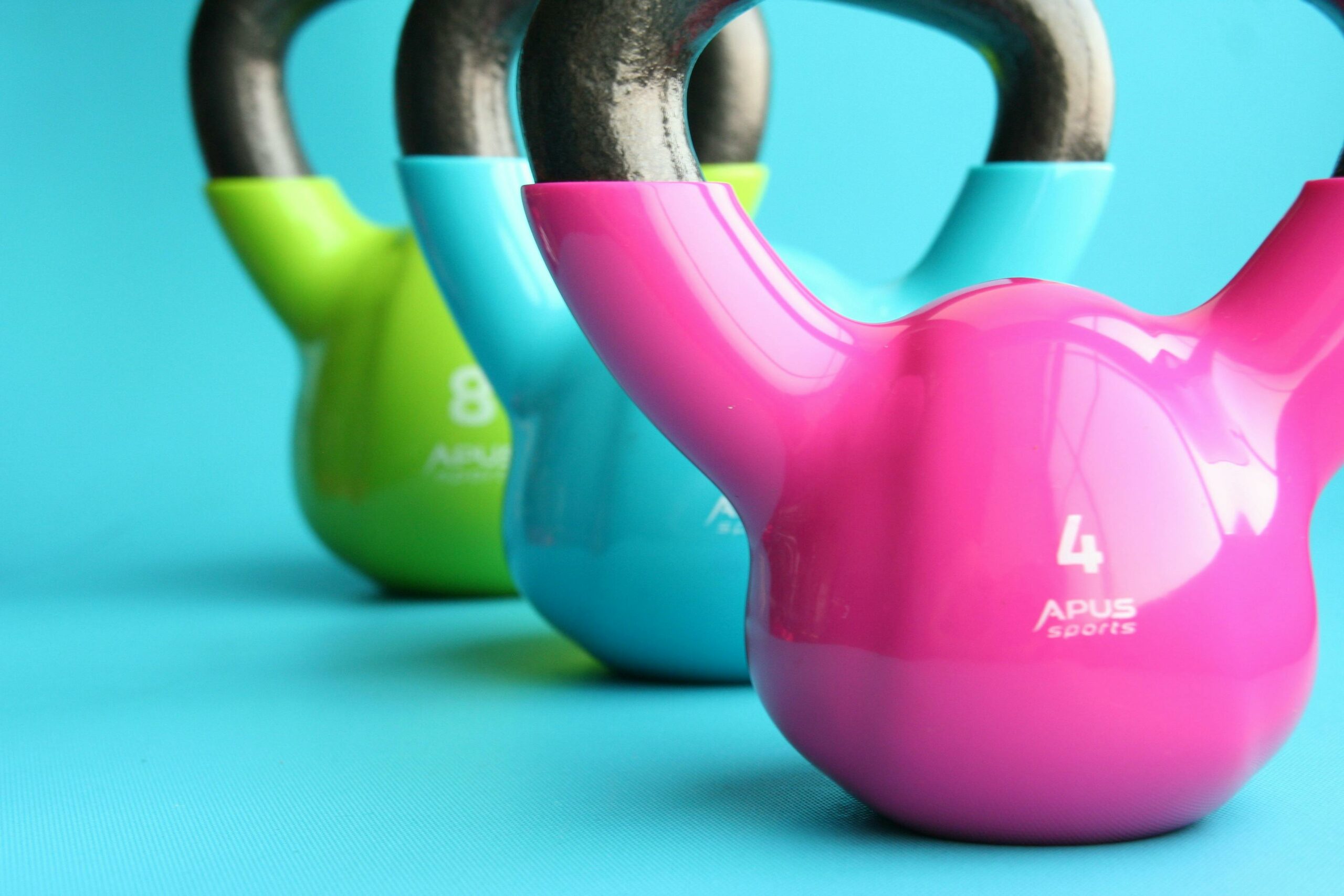 Drei bunte Kettlebells vor blauem Hintergrund