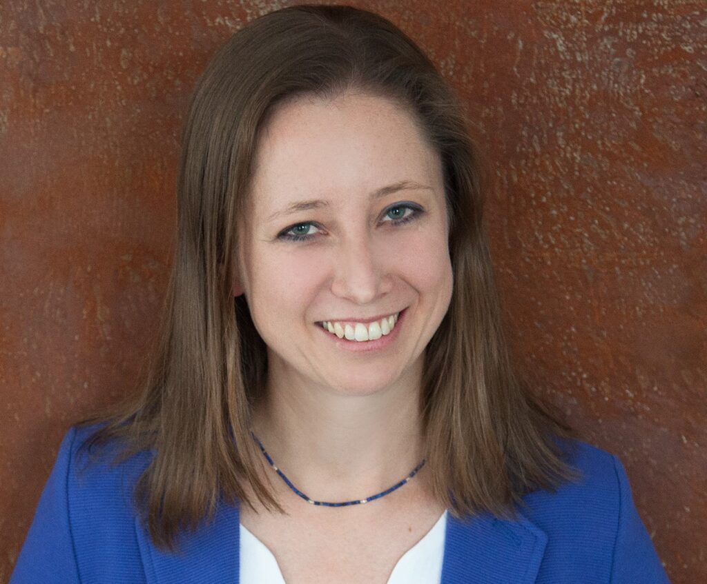 Frau in blauem Blazer vor braunem Hintergrund lächelnd