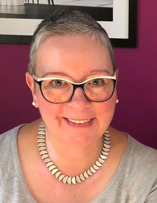 Person mit Brille und Halskette vor lila Hintergrund.