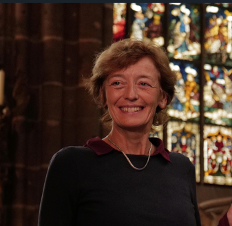 Frau lächelt in Kirche mit bunten Fenstern.