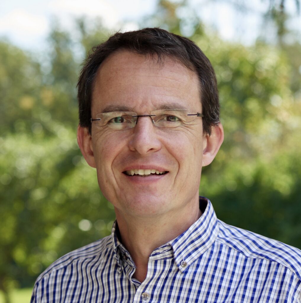 Mann im Freien mit kariertem Hemd lächelnd.