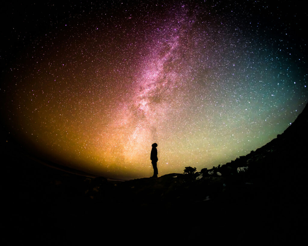 Person vor farbenfrohem Sternenhimmel und Milchstraße stehend.