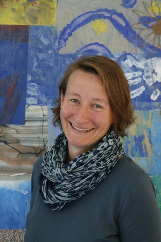 Frau vor farbenfrohem Wandbild mit Schal lächelnd