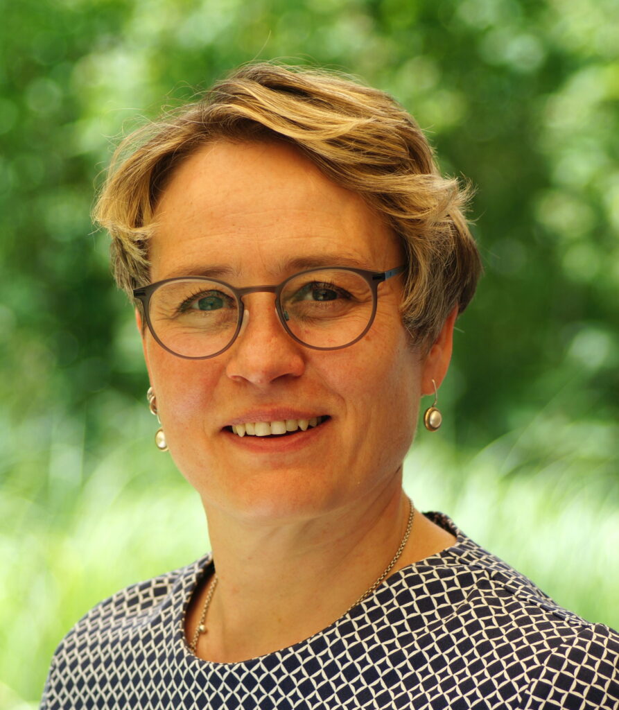 Person lächelt vor unscharfem grünen Hintergrund draußen.