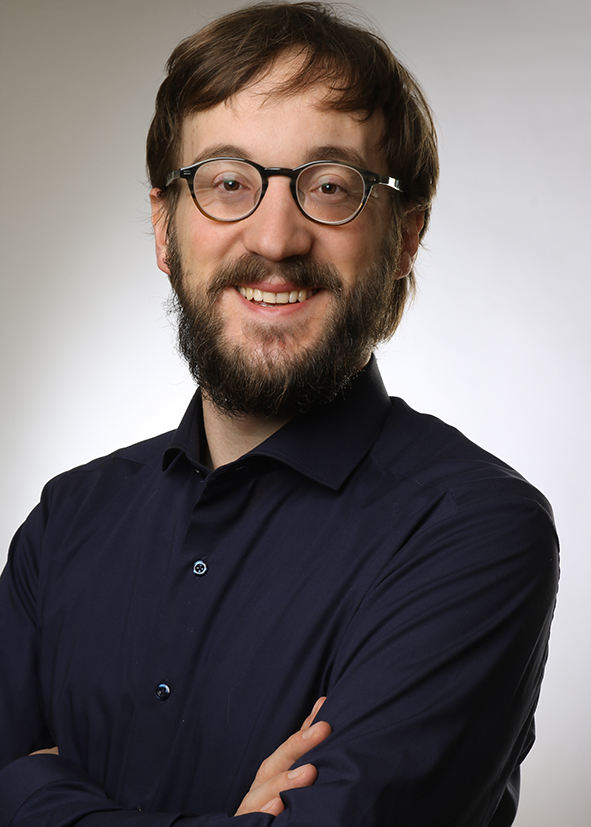 Person mit Brille und Bart in schwarzem Hemd.