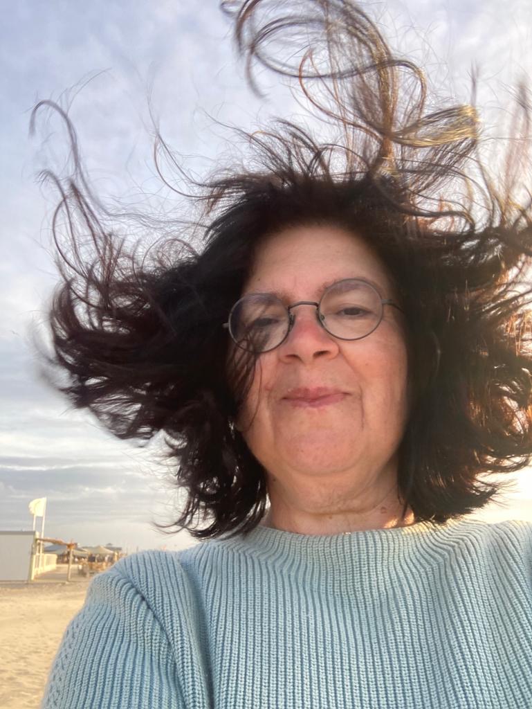 Frau mit wehendem Haar am Strand lächelnd